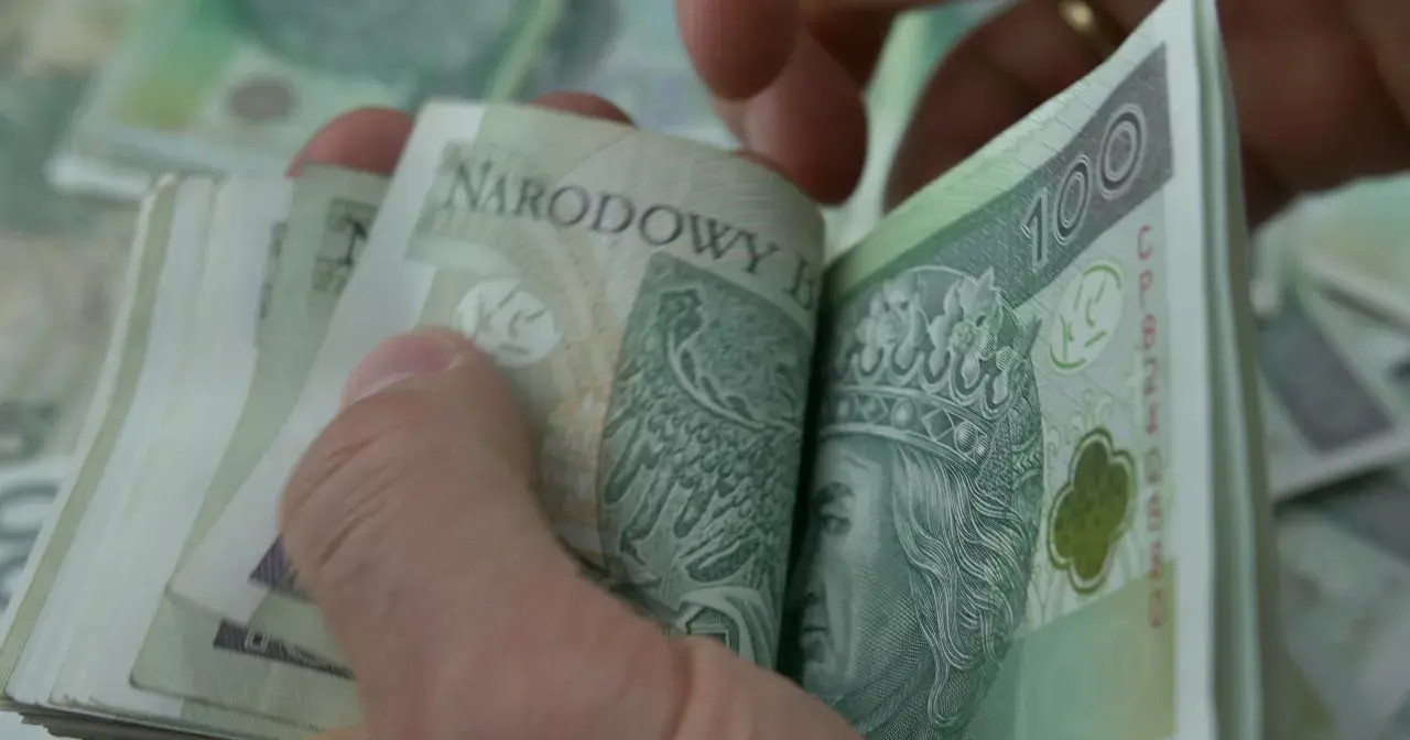 Dłonie przeglądają stos banknotów 100 zł. Może to być kwota zasiłku rehabilitacyjnego, która pomoże w powrocie do zdrowia.