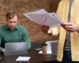 Mężczyzna w żółtej koszuli analizuje wykres, przygotowując się do rozmowy o tym, jak napisać podanie o podwyżkę.