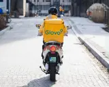 Kurier Glovo na skuterze, w żółtej kurtce z logo, przemierza ulicę. Zastanawiasz się, ile zarabia pracownik Glovo?