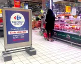 Praca w Carrefour: wykładanie towaru na ladę mięsną. W tle widać klientów i tablicę informującą o niedzielnych godzinach otwarcia.