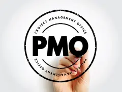 Ręka pisze markerem "PMO" w okręgu z napisem "PROJECT MANAGEMENT OFFICE". To symbol pmo stanowiska.