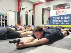 Uczestnicy kursu kpof ćwiczą pozycje strzeleckie na macie w centrum edukacji dla bezpieczeństwa.