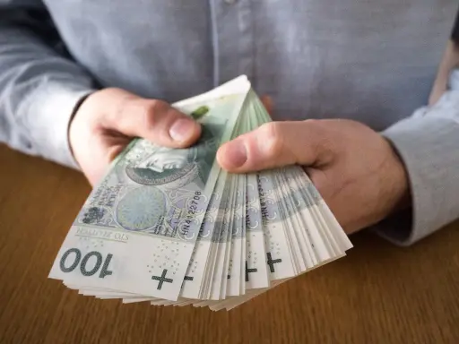 Dłonie trzymające plik banknotów 100 zł. To symbol dobrze płatnej pracy i finansowej stabilności.