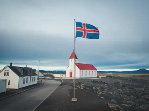 Islandia praca: biały kościół z czerwoną wieżą i flagą Islandii na tle pochmurnego nieba.