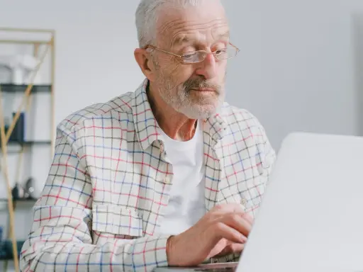 Starszy pan w okularach szuka ofert pracy dla osób po 60 roku życia na laptopie.