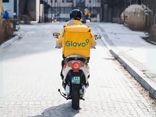 Kurier Glovo na skuterze, w żółtej kurtce z logo, przemierza ulicę. Zastanawiasz się, ile zarabia pracownik Glovo?