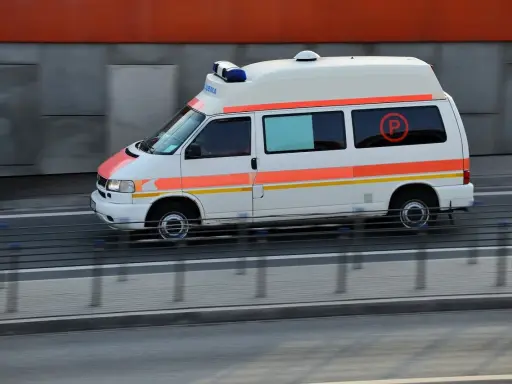 Biała karetka z pomarańczowymi pasami pędzi na sygnale. To pojazd uprzywilejowany, który może brać udział w kursie na pojazdy uprzywilejowane.
