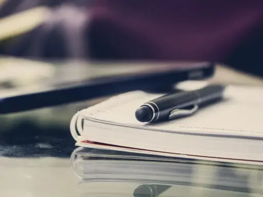 Czarny długopis spoczywa na otwartym notatniku. Obok leży laptop, gotowy do pracy. FGŚP.