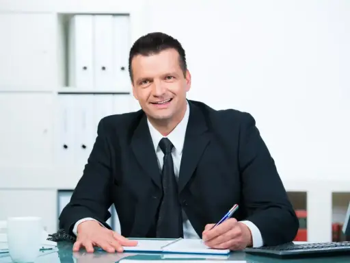 Uśmiechnięty mężczyzna w garniturze pisze w notatniku, przygotowując się do konkursu na dyrektora szkoły.