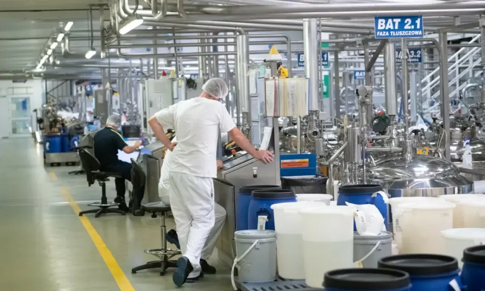 Praca w Niemczech z zakwaterowaniem: pracownicy w białych kombinezonach nadzorują produkcję w nowoczesnej fabryce.