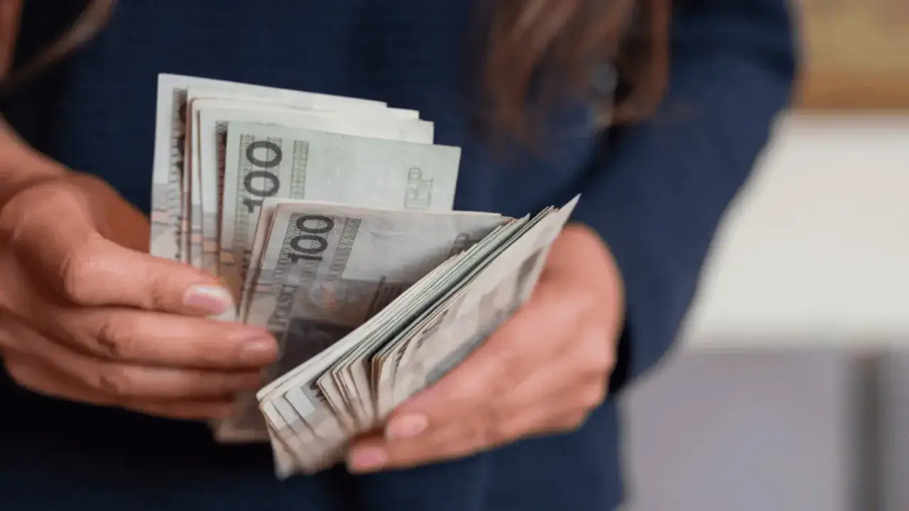 Dłonie trzymające plik banknotów 100 zł. Kto płaci macierzyński? ZUS czy pracodawca?