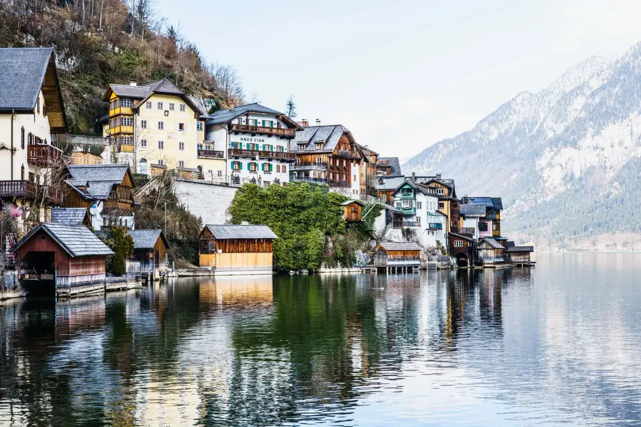 Malownicze domy nad jeziorem w Austrii, idealne na pracę z zakwaterowaniem. Góry w tle.