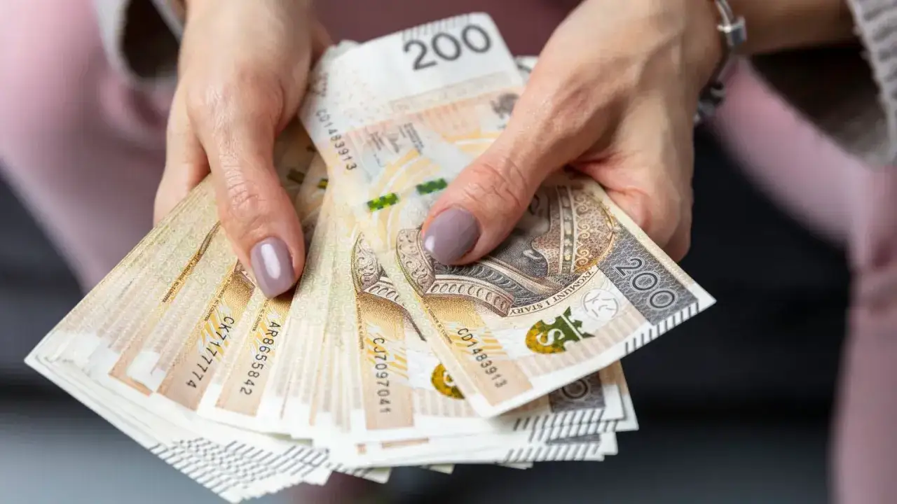Dłonie trzymają stos banknotów 200 zł. To pieniądze, które mogą pomóc w utrzymaniu rodziny, gdy ktoś płaci macierzyński.
