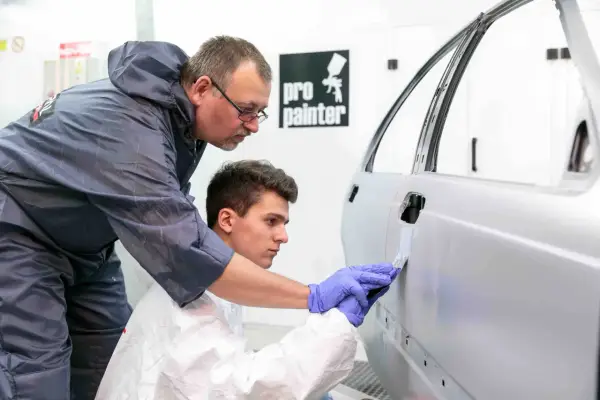 Uczeń podczas kursu lakiernika samochodowego uczy się nakładać masę szpachlową na drzwi auta pod okiem doświadczonego instruktora.