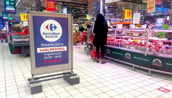 Praca w Carrefour: wykładanie towaru na ladę mięsną. W tle widać klientów i tablicę informującą o niedzielnych godzinach otwarcia.